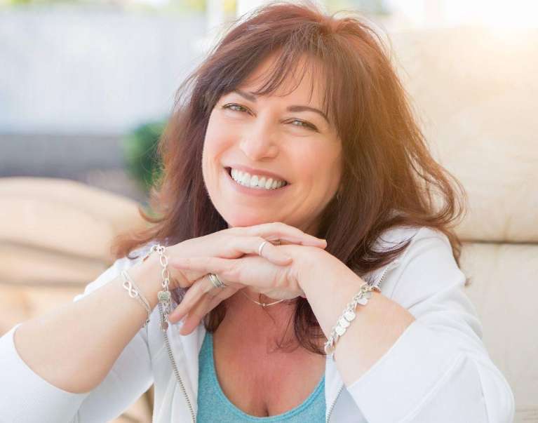 A smiling woman on a couch, showing confidence in dental implant treatment.